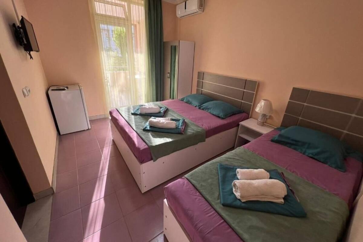 Habitació d'hotel amb dos llits, una taula petita, un armari i una finestra amb cortines.