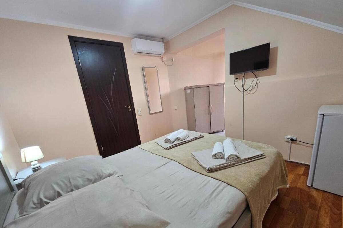 Habitació d'hotel amb dos llits, televisió, armari i una cuineta petita.