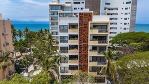 Ein mehrstöckiges Hotel mit Balkonen, einer zentralen Zierensäule und Blick auf das Meer.