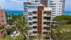 Ein mehrstöckiges Hotel mit Balkonen, einer zentralen Zierensäule und Blick auf das Meer.
