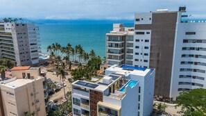 Un hotel a la costa amb diverses plantes, una piscina al terrat i vistes al mar.