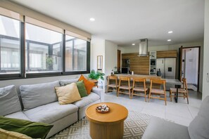 Un saló modern amb un sofà, taula de dinar amb cadires, i zona de cuina amb armaris i electrodomèstics.