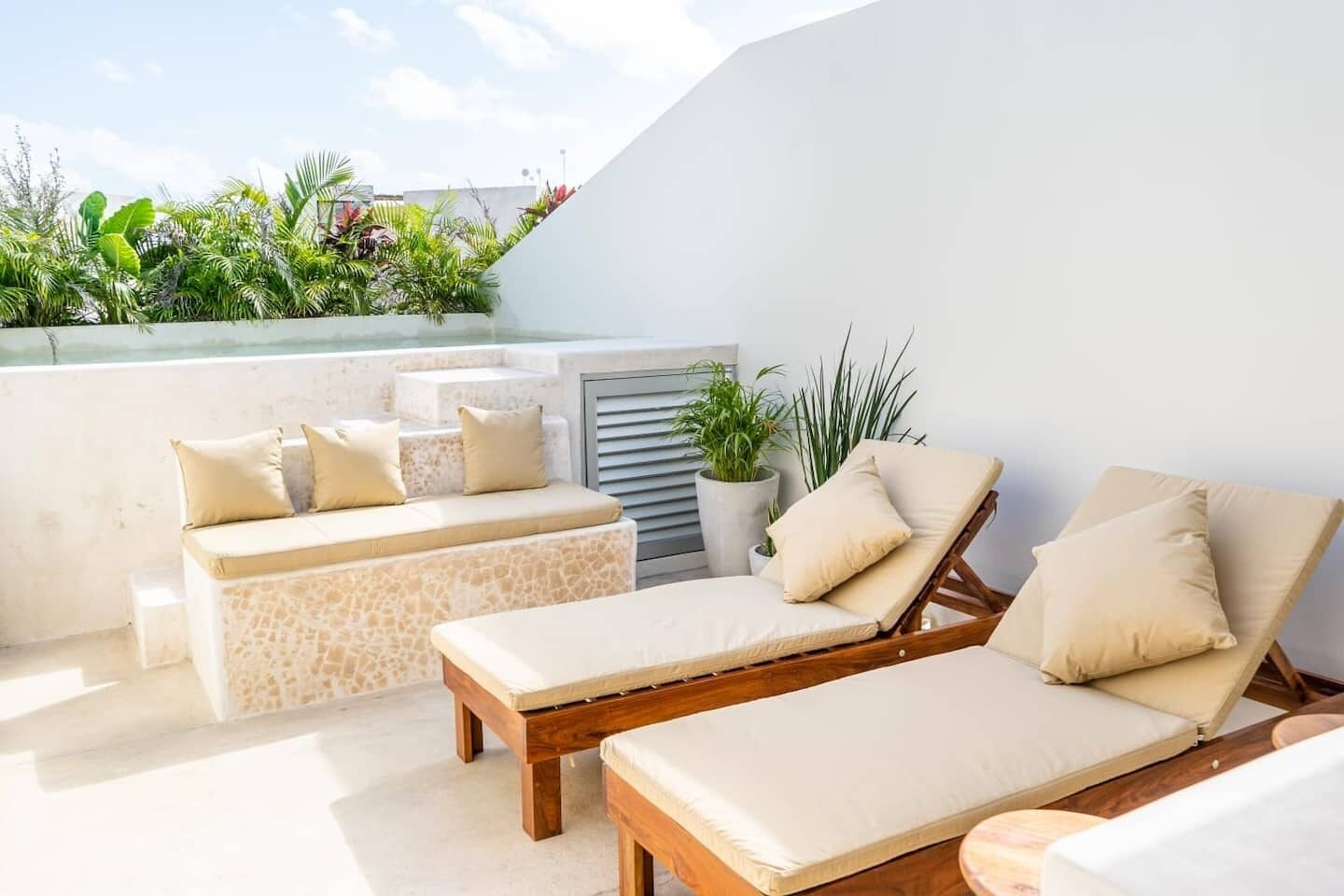 A rooftop terrace with lounge chairs, a small seating area, and potted plants.