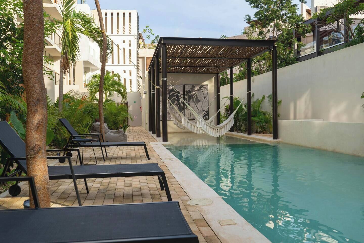 A swimming pool with lounge chairs, a hammock, and a pergola.