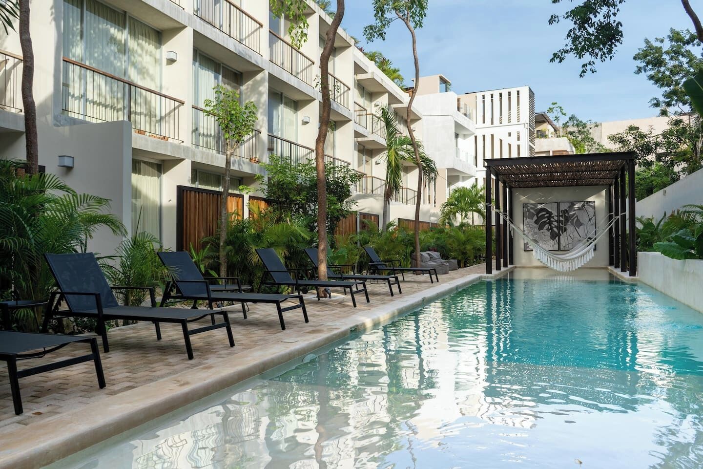 A swimming pool with lounge chairs, a hammock, and a building with balconies and a covered area.