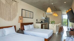 Een hotelkamer met twee bedden, een kitchenette, een eethoek en een groot raam.