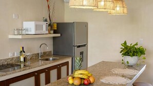 Een keuken met een centraal eiland, barstoelen, een magnetron, een koelkast en hangende hanglampen.