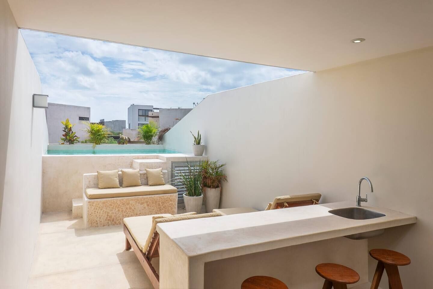 A modern kitchen with a large window overlooking a pool, a seating area with cushions, and a bar with stools.