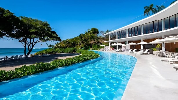 En swimmingpool med havudsigt, liggestole og en moderne bygning med store vinduer.
