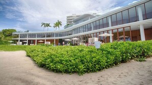Et moderne hotel med en buet glasfacade, udendørs siddepladser og en velholdt have.