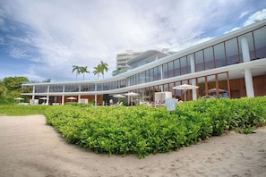 Ein modernes Hotel mit einer geschwungenen Glasfassade, Sitzgelegenheiten im Freien und einem gepflegten Garten.