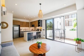 Eine moderne Küche mit einer zentralen Kochinsel, einem Essbereich mit rundem Tisch und einem Balkon mit Sitzgelegenheit.
