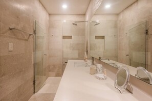 Une salle de bain moderne avec une douche à l’italienne en verre, un grand miroir et un plan de toilette blanc.