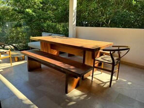 Une table de pique-nique en bois, avec des bancs et une chaise, installée sur une terrasse carrelée qui offre une vue sur les arbres.