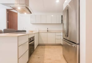 A compact kitchen with a stainless steel refrigerator, a built-in oven, and a modern light fixture. - Privileged Terrace with Hot Tub / Pool Ocean Views (Playa del Carmen)