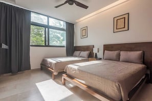 A bedroom with two beds, a ceiling fan, large windows, and artwork on the walls. - Privileged Terrace with Hot Tub / Pool Ocean Views (Playa del Carmen)
