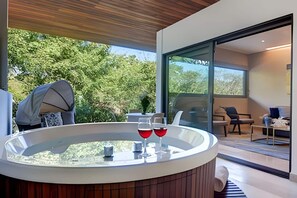 A modern outdoor hot tub area with two glasses of red wine, a wooden deck, and a glass-enclosed patio. - Privileged Terrace with Hot Tub / Pool Ocean Views (Playa del Carmen)