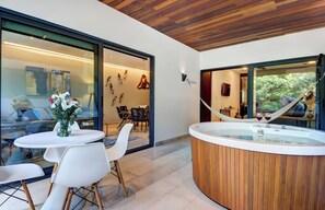 Ein modernes Interieur mit Holzbalkendecke, einem durch eine Glasschrankwand abgetrennten Essbereich und einer Wellness-Badewanne mit zwei Gläsern Rotwein.