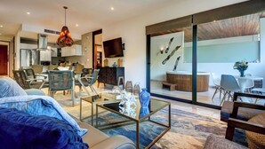 Een moderne woonkamer met een bank, salontafel en stoelen, een keuken op de achtergrond en een balkon met een eethoek.