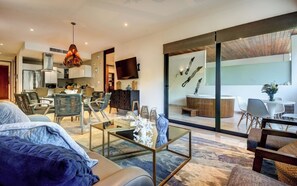 A modern living room with a sofa, coffee table, and chairs, a kitchen in the background, and a balcony with a view. - Private Hot tub-steps to the beach (Playa del Carmen)