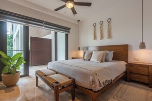 Ein Schlafzimmer mit einem großen Bett, einem Deckenventilator, einer Topfpflanze und einer Glastür.