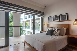 Ein modernes Schlafzimmer mit einem großen Bett, Blick auf Grünfläche und einem Balkon.