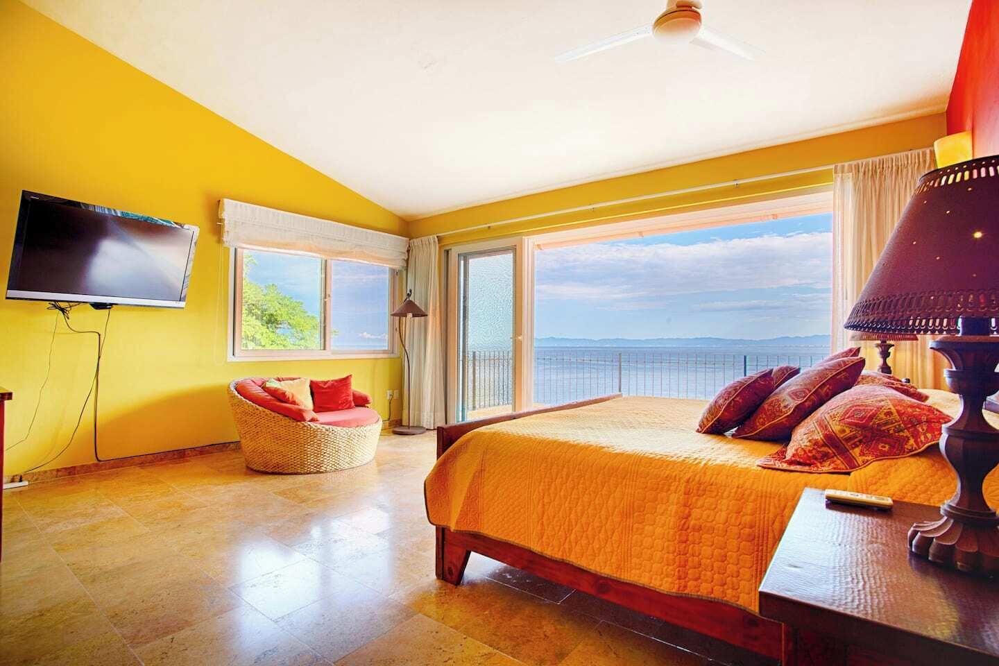 A room with a bed, a television, a chair, and a view of the sea.