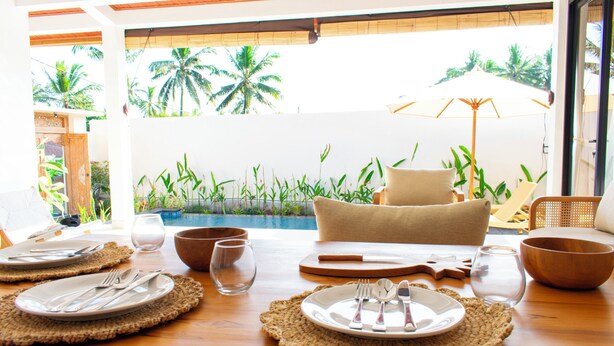 A dining table set for two with plates, cutlery, and a glass, overlooking a pool with palm trees. - 2BR Private Jungle Pool Villa in Ubud · Boho Retreat, Yoga Corner & Lush Garden (Tampaksiring)