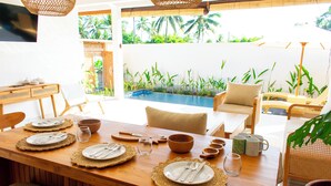 A dining area with a wooden table set for four, surrounded by chairs, with a view of a swimming pool and tropical plants. - 2BR Private Jungle Pool Villa in Ubud · Boho Retreat, Yoga Corner & Lush Garden (Tampaksiring)