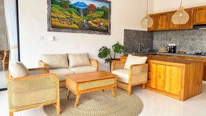 A modern living room with a sofa, chairs, a coffee table, and a kitchen area with wooden cabinets and a sink. - 2BR Private Jungle Pool Villa in Ubud · Boho Retreat, Yoga Corner & Lush Garden (Tampaksiring)