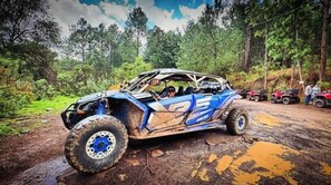 A blue off-road vehicle on a muddy path with other vehicles and people in the background.