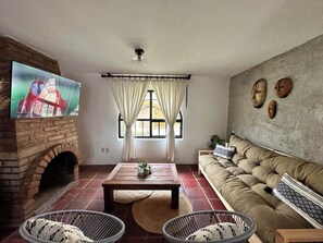 Ein Wohnzimmer mit Kamin aus Ziegelsteinen, einem Fernseher, einer Couch und einem Fenster mit Vorhängen.