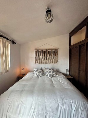 A bedroom with a bed, a wall-mounted macrame piece, a bedside lamp, and a hanging light fixture. - Comfort and Design near the Town - 3 Bedrooms (Mazamitla)