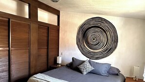 A bedroom with a bed, a wall art piece, a nightstand, and a lamp.