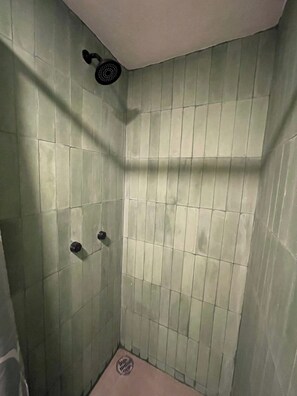 Une petite cabine de douche carrelée, équipée d’un pommeau de douche et d’un drain.