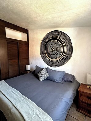 Une chambre à coucher avec un grand lit, une tête de lit en bois foncé, une œuvre d’art circulaire accrochée au mur et une table de chevet avec une lampe.