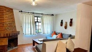 A living room with a brick fireplace, a sofa with cushions, a wooden bench, and a window with curtains. - Comfort and Design near the Town - 3 Bedrooms (Mazamitla)