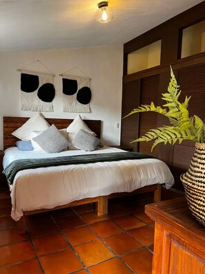 Un lit avec une tête de lit en bois, une plante sur la table de chevet et un luminaire fixé au mur.