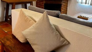 A living room with a brick fireplace, a flat-screen TV mounted on the wall, a sofa with cushions, and a wooden table. - Comfort and Design near the Town - 3 Bedrooms (Mazamitla)