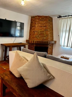 A living room with a brick fireplace, a flat-screen TV mounted on the wall, a sofa with cushions, and a wooden table. - Comfort and Design near the Town - 3 Bedrooms (Mazamitla)
