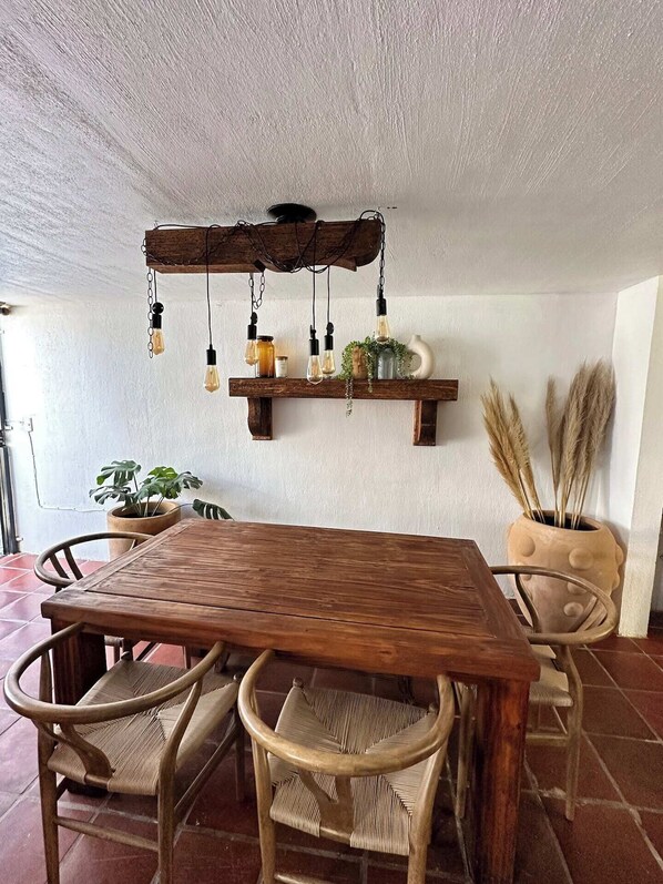 Una mesa de madera con sillas, una lámpara colgante y plantas en macetas.