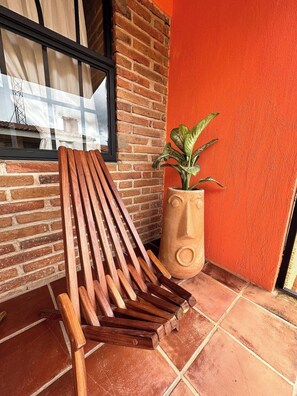 A wooden bench, a potted plant, a brick wall, and a window with curtains.