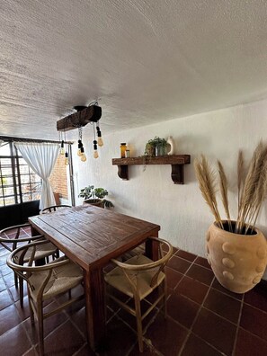 Un coin repas rustique avec une table et des chaises en bois, un luminaire suspendu et une grande plante en pot.
