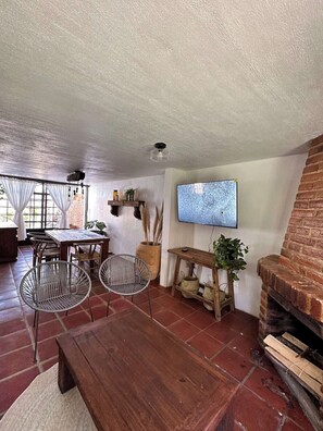 Un salon de style rustique avec une cheminée en briques, une table à manger en bois et un téléviseur fixé au mur.