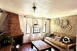 A cozy living room with a brick fireplace, a wooden coffee table, a sofa with cushions, and a wall decorated with woven plates.