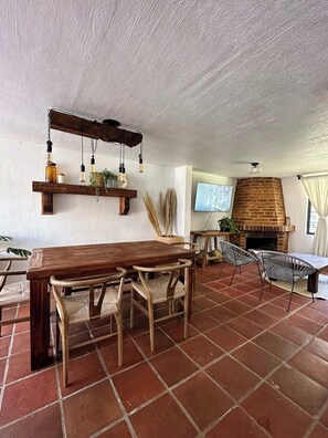 Un comedor con una mesa y sillas de madera, una lámpara colgante y una chimenea de ladrillo.