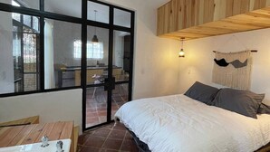A bedroom with a bed, a window, a wooden ceiling, and a bathroom with a bathtub.