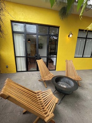 Un bâtiment jaune doté d’un patio aménagé avec des fauteuils en bois et un foyer extérieur.