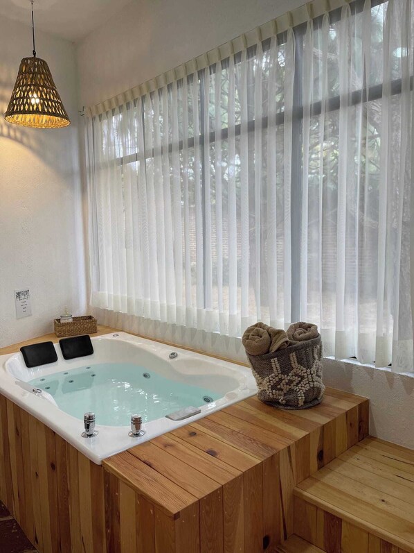 Une baignoire en bois dotée d’un siège intégré, un panier en osier contenant des serviettes et un luminaire suspendu.