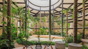 A spacious indoor garden with a central seating area, surrounded by lush greenery and a circular ceiling structure. - Ixchel Luxury PH Studio Priv Rooftop Pool 150 WiFi (Tulum)